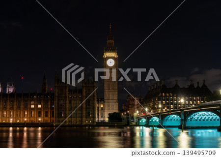 Bright clock face rises above the river and bridge at night, combining urban skyline with time concept and travel destination atmosphere. Bright clock face rises above the river and bridge at night, combining urban skyline with time concept and travel destination atmosphere. 139495709
