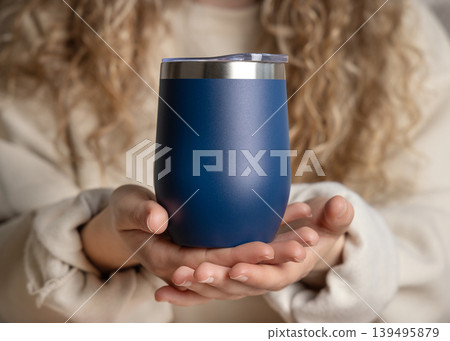 Blank dark blue 12 oz wine tumbler mockup in hands of woman in beige sweatshirt, copy space Blank dark blue 12 oz wine tumbler mockup in hands of woman in beige sweatshirt, copy space 139495879