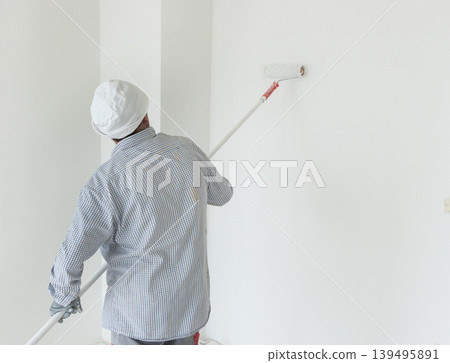 Male worker painting white wall with roller in empty room, back view. Finishing works in apartment 139495891