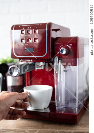 Hand holding cup of fresh espresso coffee from red coffee machine at home Hand holding cup of fresh espresso coffee from red coffee machine at home 139495952