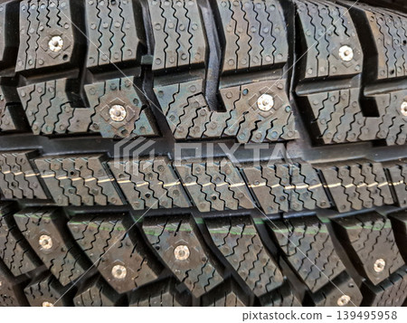 A close view of a studded winter tire shows the tread pattern built for grip and traction in snow and ice. This design helps improve safety while driving in harsh winter weather. 139495958