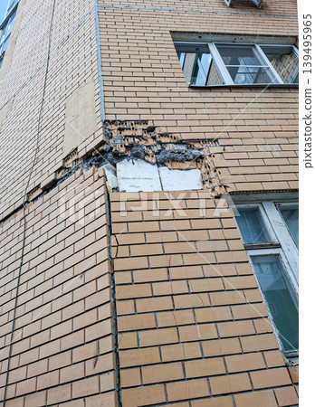 A corner of a modern residential building shows severe damage to the brickwork. The brick is missing, exposing styrofoam insulation. This area requires urgent repair. A corner of a modern residential building shows severe damage to the brickwork. The brick is missing, exposing styrofoam insulation. This area requires urgent repair. 139495965