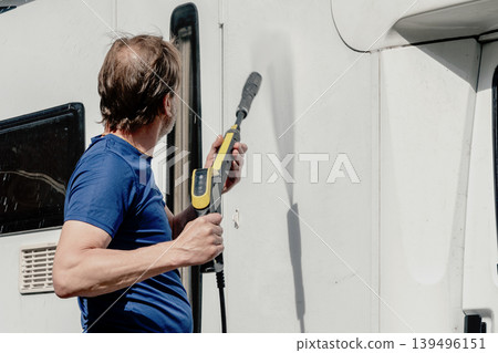 Man cleaning white motorhome surface with pressure washer near garage in summer. 139496151