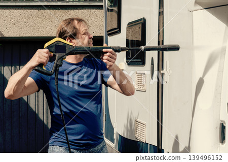 Man washing white residential motorhome with powerful water spray near private house. 139496152