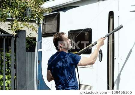 Man cleaning white motorhome with pressure washer outdoors on sunny day. 139496160