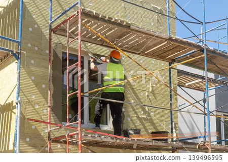 Professional Construction Worker Installing Wall Insulation on Scaffolding Professional Construction Worker Installing Wall Insulation on Scaffolding 139496595