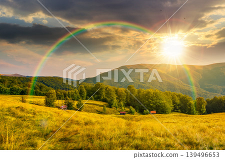 sunset over mountainous rural landscape in summertime. picturesque highland woods and grassy meadow. view of countryside scenery with forested hills behind the pasture under rainbow sunset over mountainous rural landscape in summertime. picturesque highland woods and grassy meadow. view of countryside scenery with forested hills behind the pasture under rainbow 139496653