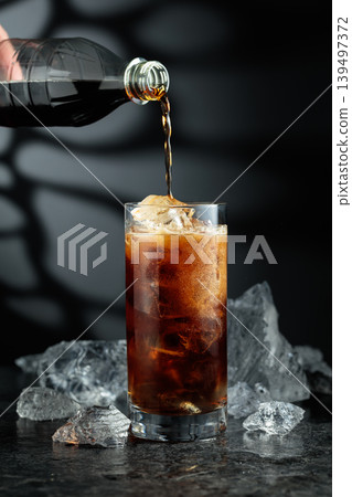 Cola is poured into a glass with ice. Cola is poured into a glass with ice. 139497372