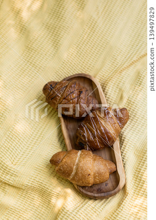 Freshly baked plain and glazed croissants on wooden tray outdoors on textured fabric Freshly baked plain and glazed croissants on wooden tray outdoors on textured fabric 139497829