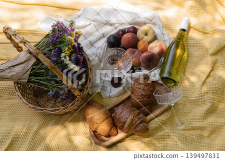 Elegant picnic spread with wine, fresh fruits, and croissants on a yellow blanket outdoors Elegant picnic spread with wine, fresh fruits, and croissants on a yellow blanket outdoors 139497831