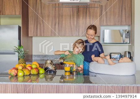 Mother and son preparing smoothie in kitchen while baby lies in cozy lounger on table watching. Family cooking together, healthy lifestyle, parenting, sibling bonding and everyday life concept Mother and son preparing smoothie in kitchen while baby lies in cozy lounger on table watching. Family cooking together, healthy lifestyle, parenting, sibling bonding and everyday life concept 139497914