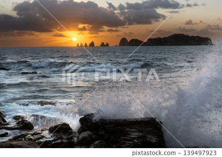 A view of the sunrise over the Nanatsu-iwa rocks off the coast of Hyuga-nada Sea and the crashing waves from Inozakibana Park Campground in Nichinan City, Miyazaki Prefecture. A view of the sunrise over the Nanatsu-iwa rocks off the coast of Hyuga-nada Sea and the crashing waves from Inozakibana Park Campground in Nichinan City, Miyazaki Prefecture. 139497923