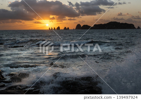 A view of the sunrise over the Nanatsu-iwa rocks off the coast of Hyuga-nada Sea and the crashing waves from Inozakibana Park Campground in Nichinan City, Miyazaki Prefecture. A view of the sunrise over the Nanatsu-iwa rocks off the coast of Hyuga-nada Sea and the crashing waves from Inozakibana Park Campground in Nichinan City, Miyazaki Prefecture. 139497924