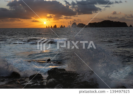 A view of the sunrise over the Nanatsu-iwa rocks off the coast of Hyuga-nada Sea and the crashing waves from Inozakibana Park Campground in Nichinan City, Miyazaki Prefecture. 139497925