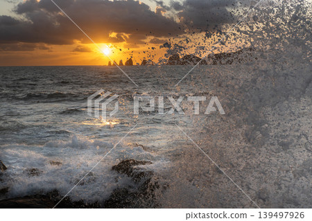 A view of the sunrise over the Nanatsu-iwa rocks off the coast of Hyuga-nada Sea and the crashing waves from Inozakibana Park Campground in Nichinan City, Miyazaki Prefecture. 139497926