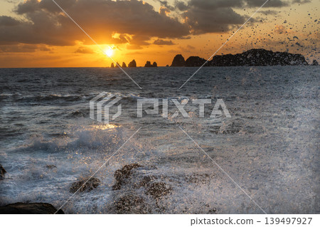 A view of the sunrise over the Nanatsu-iwa rocks off the coast of Hyuga-nada Sea and the crashing waves from Inozakibana Park Campground in Nichinan City, Miyazaki Prefecture. A view of the sunrise over the Nanatsu-iwa rocks off the coast of Hyuga-nada Sea and the crashing waves from Inozakibana Park Campground in Nichinan City, Miyazaki Prefecture. 139497927