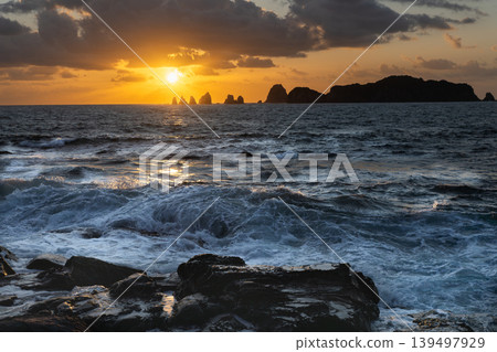 A view of the sunrise over the Nanatsu-iwa rocks off the coast of Hyuga-nada Sea and the crashing waves from Inozakibana Park Campground in Nichinan City, Miyazaki Prefecture. 139497929