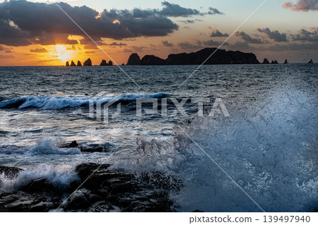 A view of the sunrise over the Nanatsu-iwa rocks off the coast of Hyuga-nada Sea and the crashing waves from Inozakibana Park Campground in Nichinan City, Miyazaki Prefecture. A view of the sunrise over the Nanatsu-iwa rocks off the coast of Hyuga-nada Sea and the crashing waves from Inozakibana Park Campground in Nichinan City, Miyazaki Prefecture. 139497940