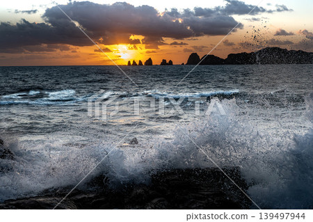 A view of the sunrise over the Nanatsu-iwa rocks off the coast of Hyuga-nada Sea and the crashing waves from Inozakibana Park Campground in Nichinan City, Miyazaki Prefecture. A view of the sunrise over the Nanatsu-iwa rocks off the coast of Hyuga-nada Sea and the crashing waves from Inozakibana Park Campground in Nichinan City, Miyazaki Prefecture. 139497944