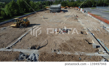 Aerial view of a construction site with heavy machinery and building foundations under development. Aerial view of a construction site with heavy machinery and building foundations under development. 139497948