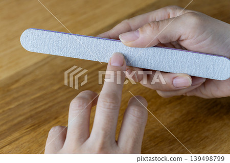 A woman is using a nail file to trim her fingernails. A woman is using a nail file to trim her fingernails. 139498799