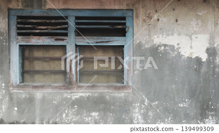 A worn blue window in a cracked concrete wall with peeling paint and a classic texture. 139499309