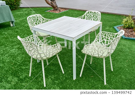 Stylish outdoor dining set on artificial grass with landscaping elements. Stylish outdoor dining set on artificial grass with landscaping elements. 139499742