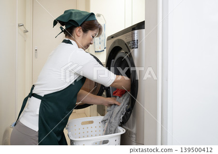 一位做家事的婦女正在把髒衣服放進洗衣機。 一位做家事的婦女正在把髒衣服放進洗衣機。 139500412