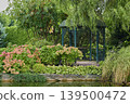 Serene garden gazebo surrounded by vibrant flowers and lush greenery in bright daylight 139500472