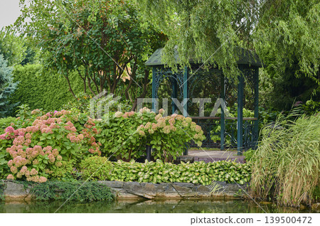 Serene garden gazebo surrounded by vibrant flowers and lush greenery in bright daylight Serene garden gazebo surrounded by vibrant flowers and lush greenery in bright daylight 139500472