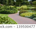 Brick pathway weaves through lush greenery in a serene garden landscape 139500477