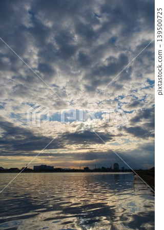 Sunset over the riverbank and cityscape, with rays of sunlight streaming down from between the clouds. Sunset over the riverbank and cityscape, with rays of sunlight streaming down from between the clouds. 139500725