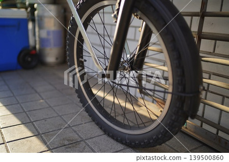 The tiled floor of the bicycle parking area and the front wheel of a bicycle, illuminated by the setting sun. The tiled floor of the bicycle parking area and the front wheel of a bicycle, illuminated by the setting sun. 139500860