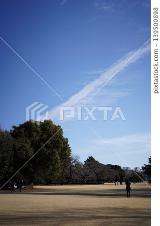 A long, straight contrail stretches across the winter blue sky, and the park square. A long, straight contrail stretches across the winter blue sky, and the park square. 139500898