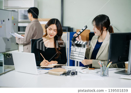 Creative team planning video production in modern office, using clapperboard, laptop and notebook. Business, marketing, content creation Creative team planning video production in modern office, using clapperboard, laptop and notebook. Business, marketing, content creation 139501839