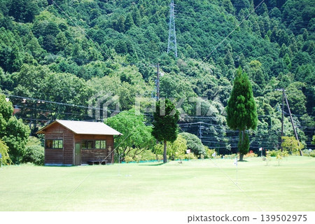 A wooden cabin nestled in a grassy field amidst lush green mountains. A wooden cabin nestled in a grassy field amidst lush green mountains. 139502975