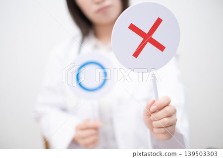A female doctor holds up a sign indicating incorrect answer. A female doctor holds up a sign indicating incorrect answer. 139503303