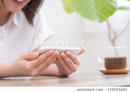 A woman holding her smartphone horizontally in the living room. 139503608