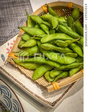 Close up of a woven basket filled with fresh, salted edamame pods 139503814