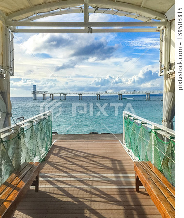Ocean pier in Japan Okinawa with benches and blue sky, leading to a distant structure over the water 139503815