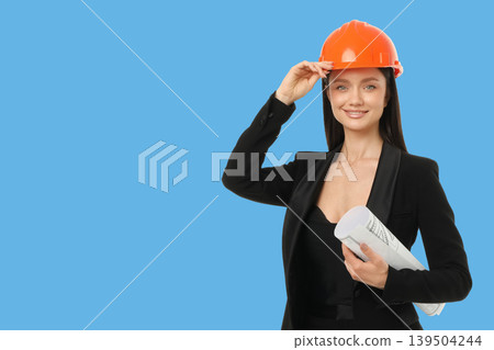 Worker holds blueprints and adjusts her hard hat in office Worker holds blueprints and adjusts her hard hat in office 139504244