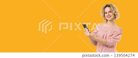 Woman smiles while holding smartphone with a bright background Woman smiles while holding smartphone with a bright background 139504274