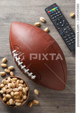 A football sits on a table with pistachios and a remote A football sits on a table with pistachios and a remote 139504360