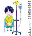 An image of a child sitting in a chair with an IV drip in their left arm, smiling and reading a book propped up against the chair. 139504565