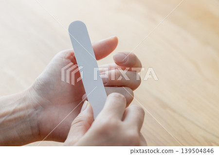 一位女士正在用指甲銼修剪指甲。 一位女士正在用指甲銼修剪指甲。 139504846