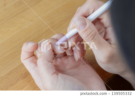 一位女士正在使用角質層推棒推回指甲角質層。這是她自己進行指甲護理的方式。 一位女士正在使用角質層推棒推回指甲角質層。這是她自己進行指甲護理的方式。 139505332