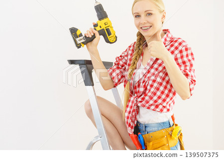 Woman on ladder using drill 139507375