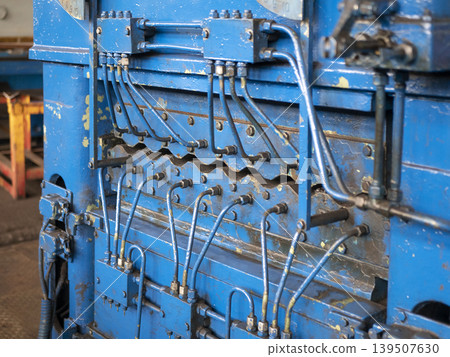 Close-up of a blue industrial metal leveler machine with a complex hydraulic system of pipes and valves. Heavy-duty manufacturing equipment 139507630