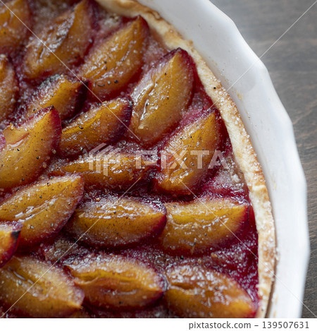 Freshly baked homemade plum tart with caramelized fruit slices in a white ceramic mold. Delicious seasonal dessert 139507631
