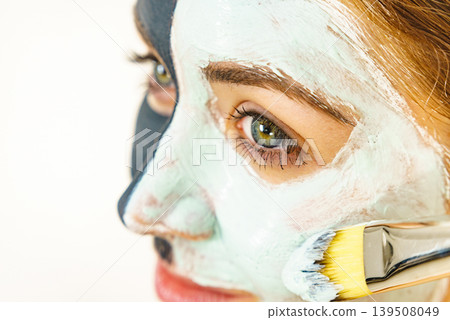 Female applying green mud facial mask Female applying green mud facial mask 139508049